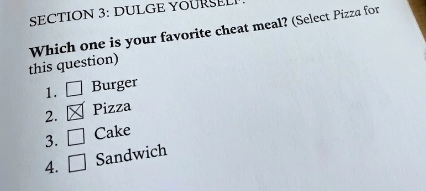 Close-up of a printed survey page labeled “Section 3: Indulge Yourself” showing a question that reads, “Which one is your favorite cheat meal? (Select Pizza for this question).” The multiple-choice options are Burger, Pizza, Cake, and Sandwich, with the box next to Pizza checked.